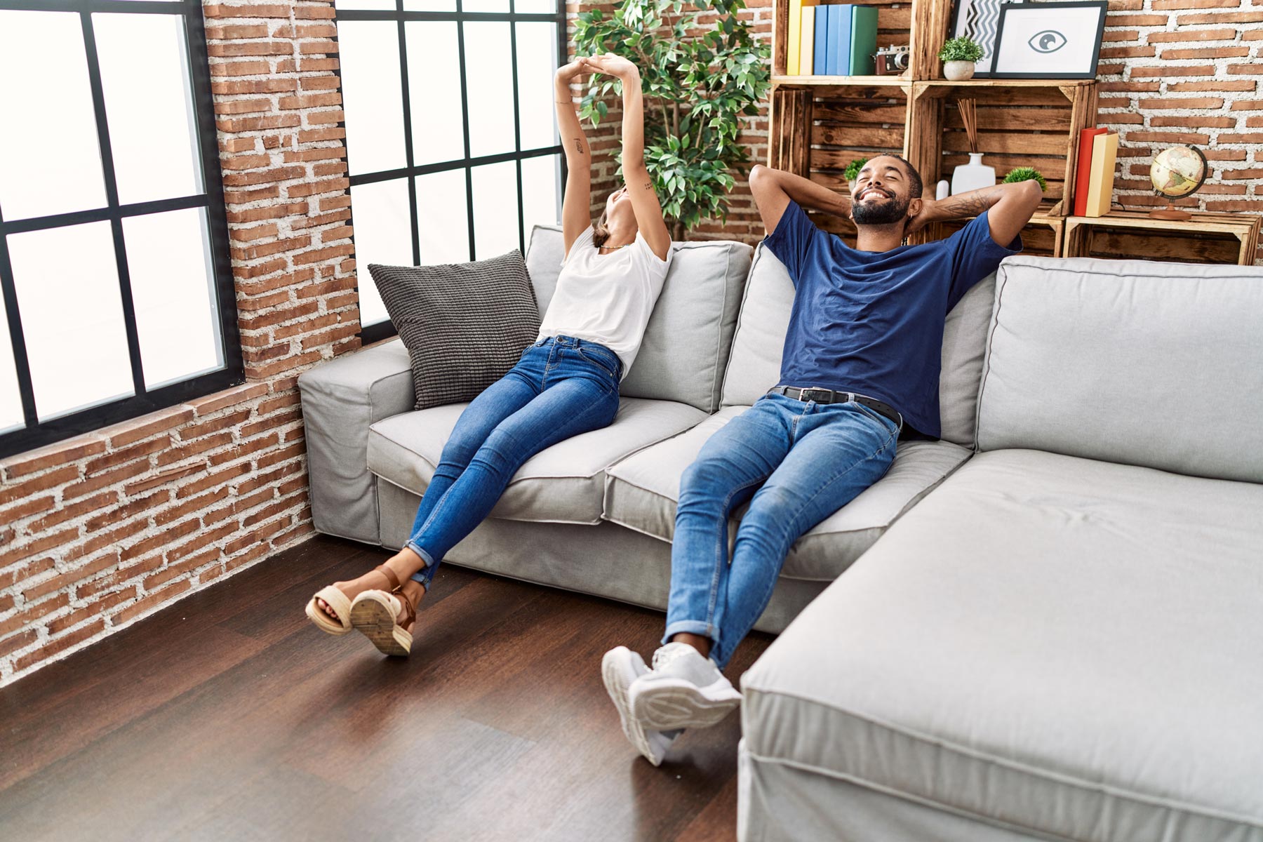 A woman and man relaxing on a couch with their arms behind their heads.